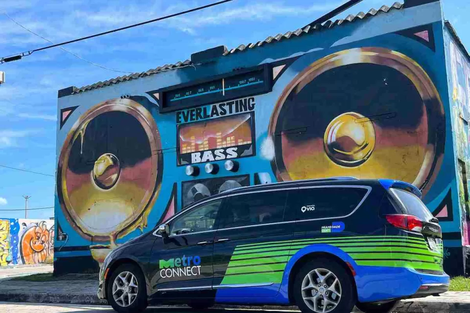 Black and green MetroConnect microtransit van in front of mural of boom box on Miami building.